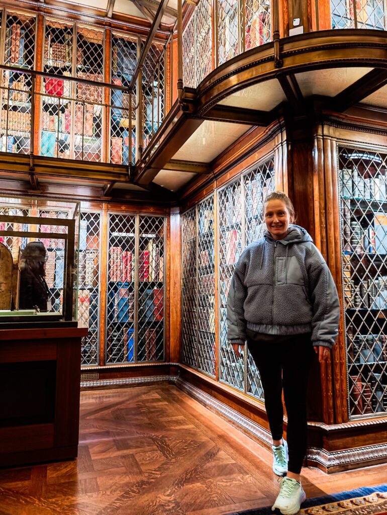 Me standing inside the Morgan Library in a blue fleece with stacks of vintage books behind me. 