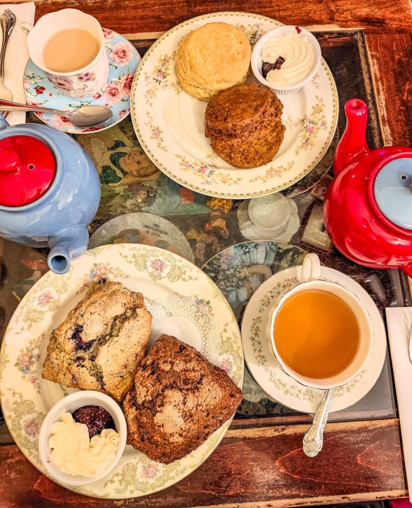 Aerial view of tea in white cups and scones on small plates with jam and cream and red and blue tea pots at Alice's Tea Cup. 