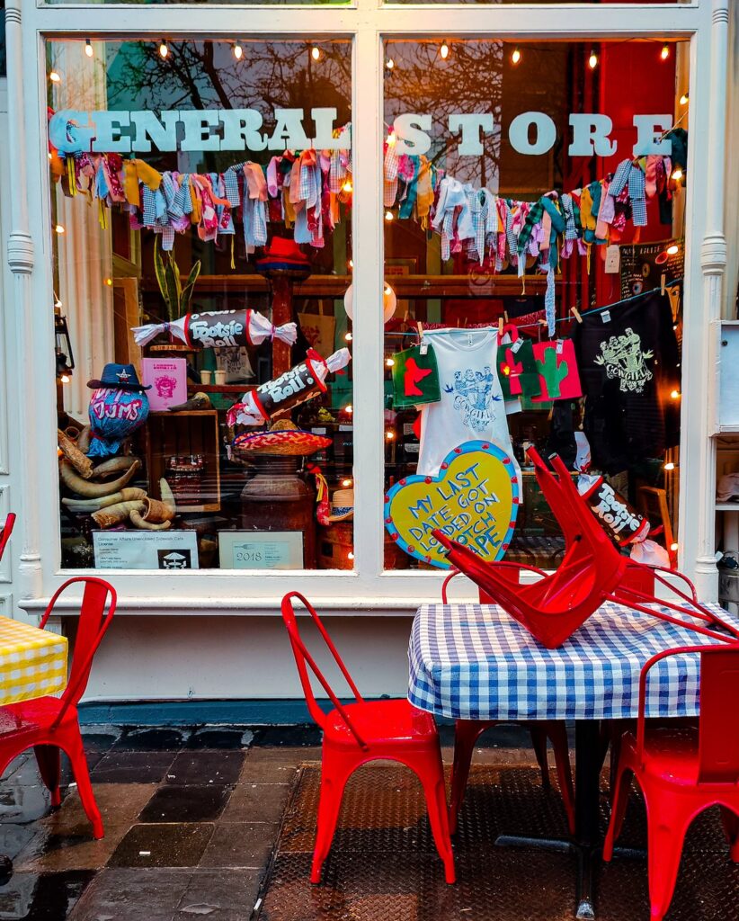 Exterior view of Cow Girl with clothes hanging in the window and lights and the words "General Store" written out front. 