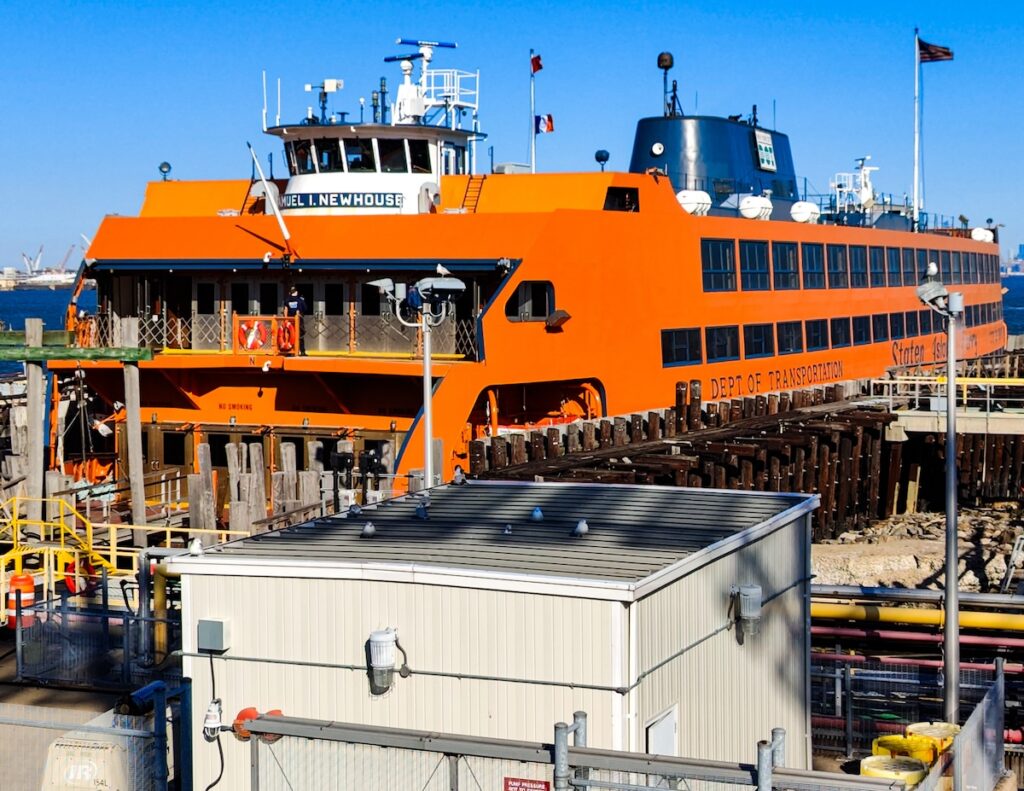 View of the orange Staten Island Ferry docked at a harbor in Staten Island on a sunny day. 