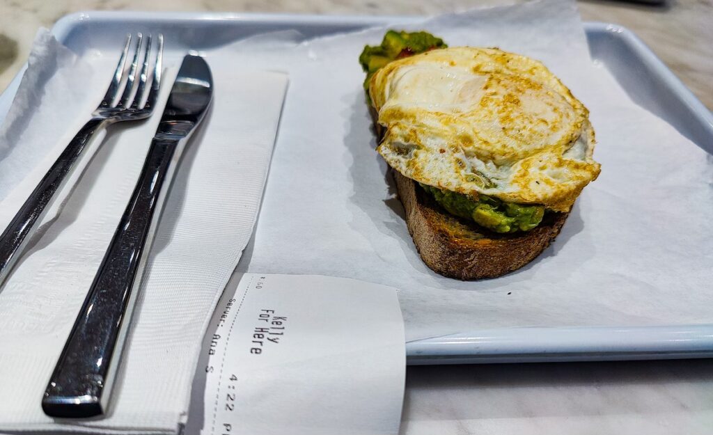 View of my avocado toast with a poached egg and silverware on a metal tray from daily Provisions. 