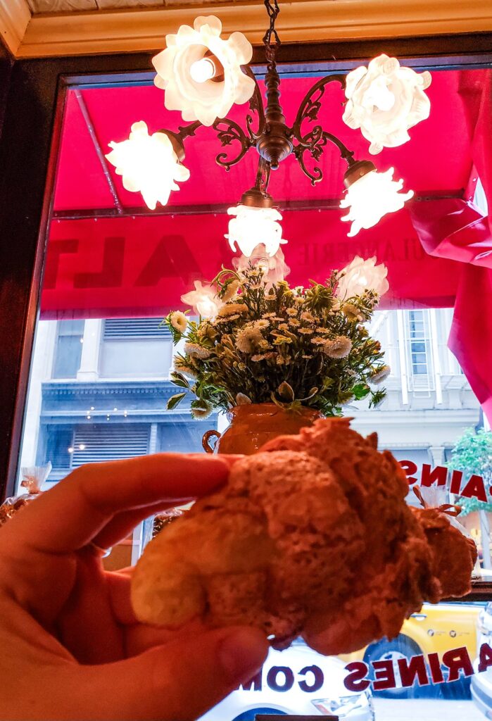 Me holding a croissant in Balthazar with vintage white lights hanging from a chandelier on the ceiling. It's one of the best bakeries in NYC. 