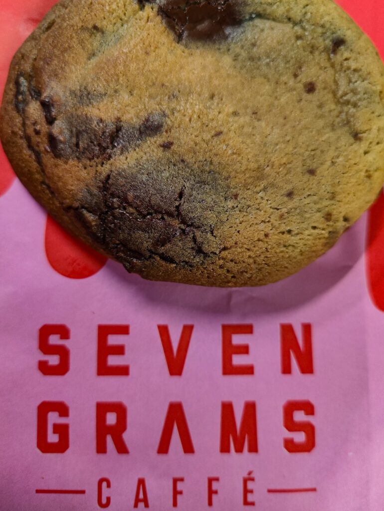 View of the legendary chocolate chip cookie from Seven Grams Caffe. It's on a pink and red plastic wrapper that says "Seven Grams".