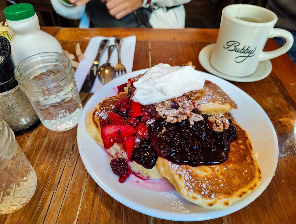 View of a giant plate of pancakes from Bubby's with whipped cream and berries on top.