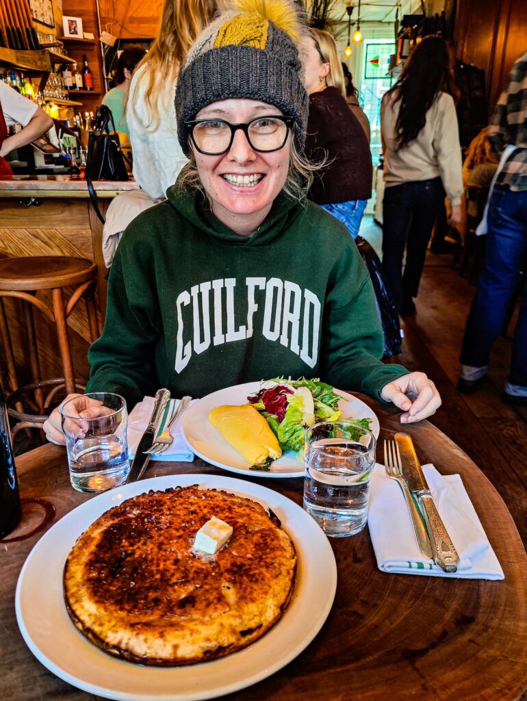 View of me sitting in a green sweatshirt and a winter hat with an omelet and pancakes on the table in front me at Vinegar Hill House. 