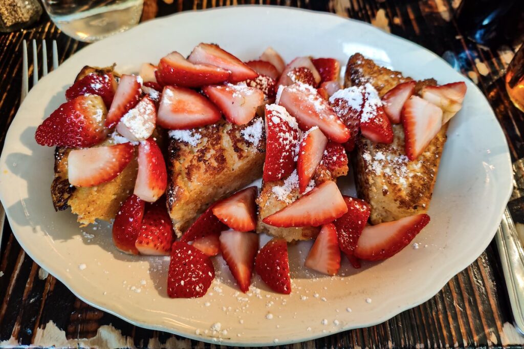 An aerial view of a plate of French Toast topped with strawberries and powdered sugar from Jacob's Pickles. 