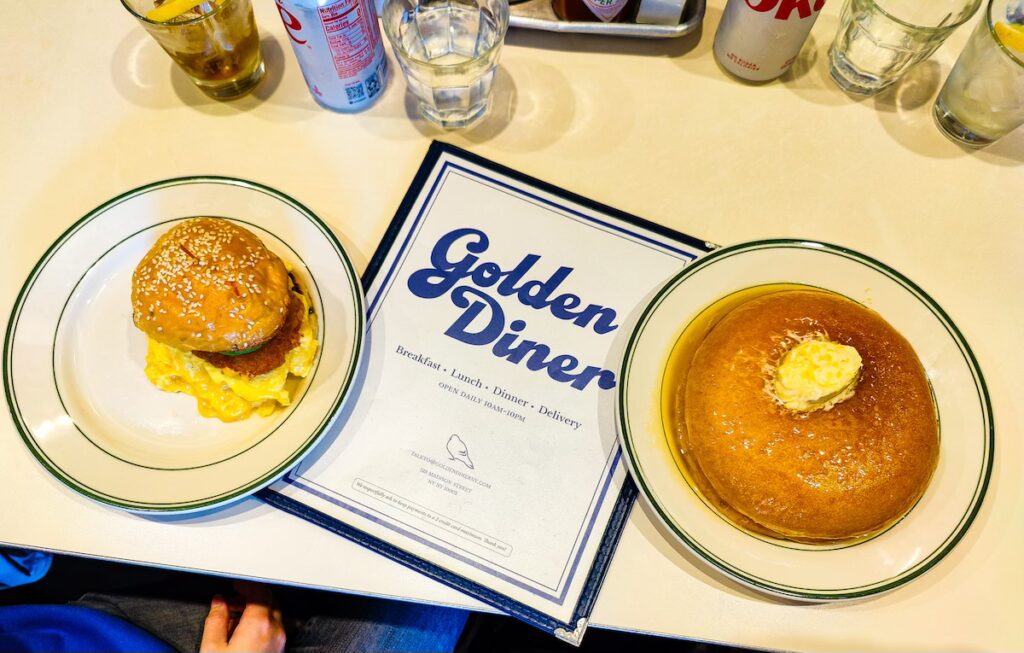 Aerial view of a breakfast sandwich and pancakes on a white table with the Golden Diner menu in the middle of this restaurant.