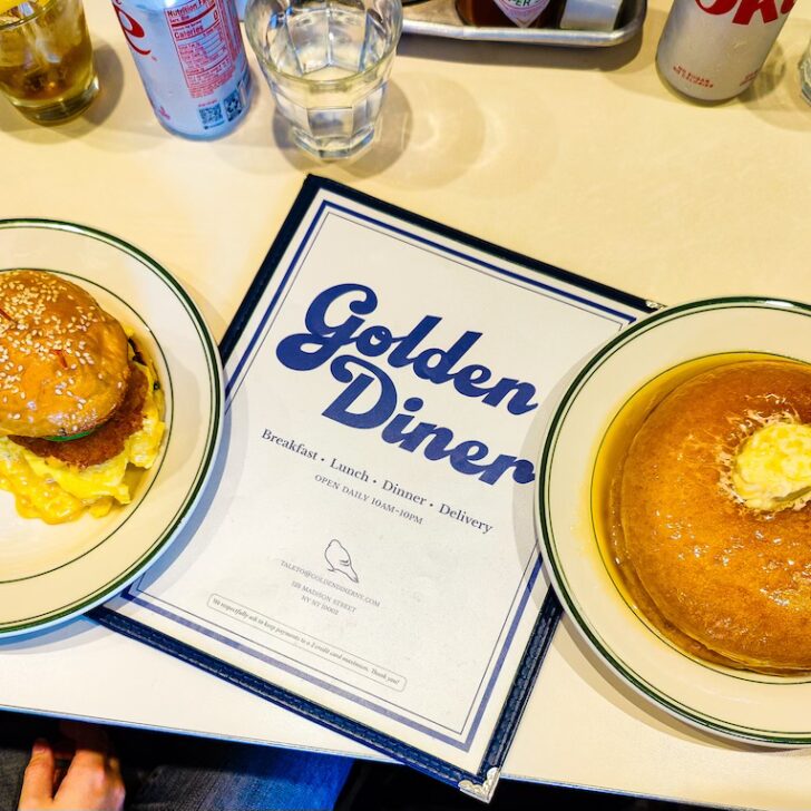 Aerial view of a breakfast sandwich and pancakes on a white table with the Golden Diner menu in the middle of this restaurant.