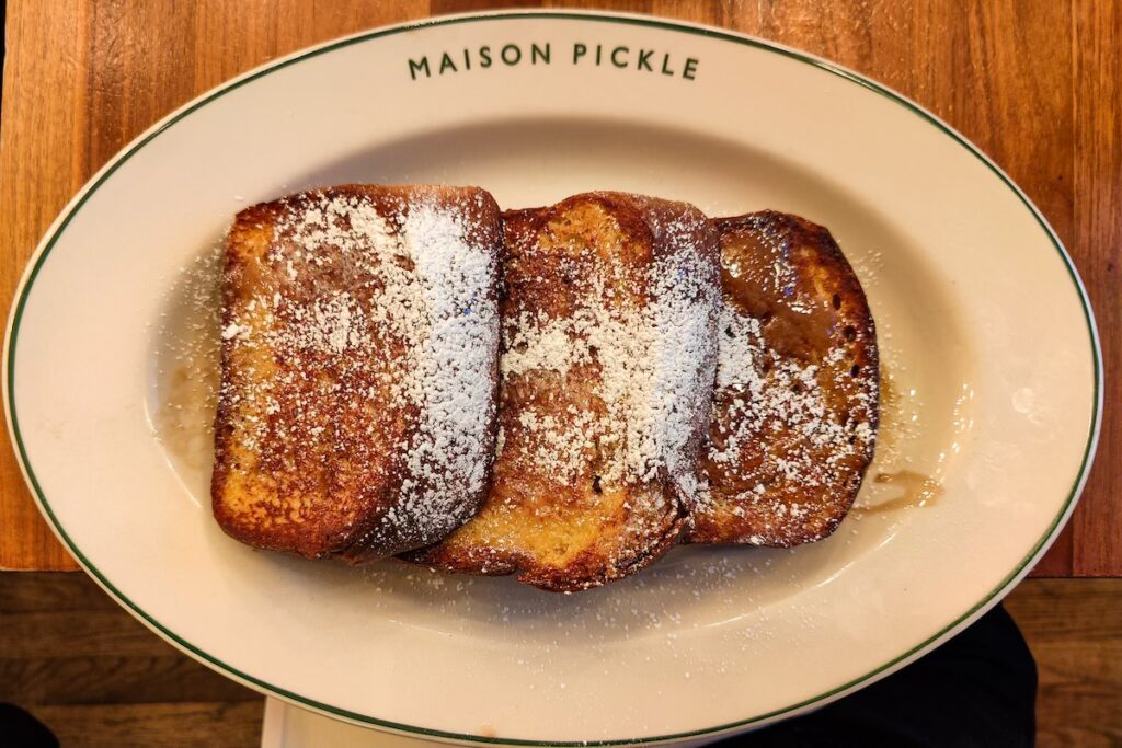 Aerial view of the classic french Toast with powdered sugar on a plate that says, "Maison Pickle". 