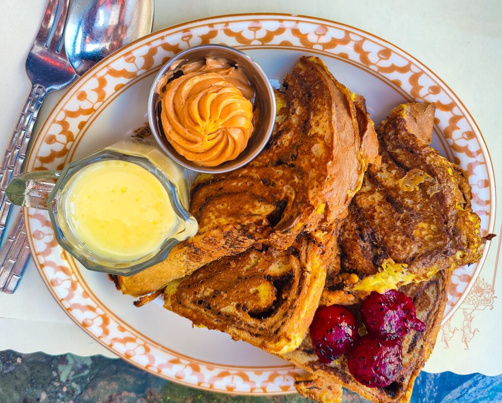 Aerial view of the French toast at Thai Diner. You can see a Thai Tea cream spread and condensed milk on the side on a white plate. This is the best French toast in NYC. 